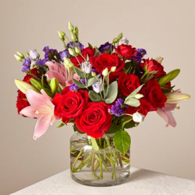 Share a smile with your loved ones through a bouquet filled with stunning beauty and heartfelt joy. Comprised of vivid red roses, purple double lisianthus, pink lilies and red spray roses within a clear glass vase, vibrant color bursts from every bloom.