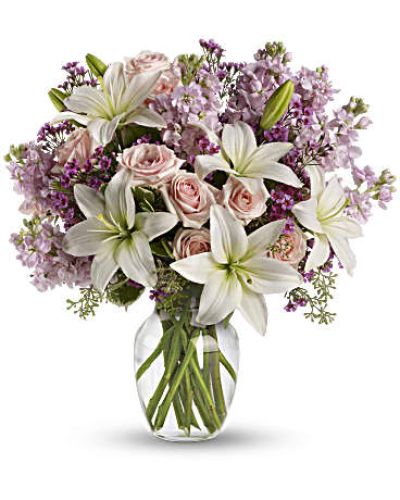 <p>A gentle mix of light pink spray roses, white Asiatic lilies, lavender stock, and sprigs of lavender waxflower creates a soothing palette of pastel tones. Lush greenery adds contrast and structure, while a clear glass vase completes the look with understated refinement.</p>