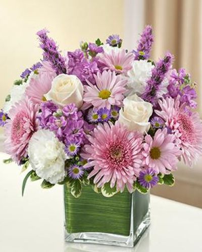 <p>This bouquet features a soothing mix of lavender roses, white stock, liatris, cremones, white carnations, daisy poms, and monte casino asters. Arranged in a clear glass cube vase lined with a natural Ti leaf ribbon, the design is compact yet expressive.</p>