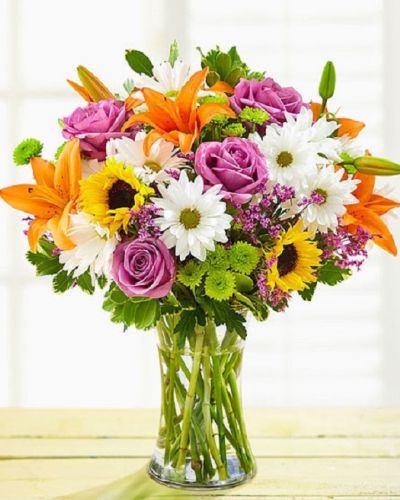 <p>This joyful bouquet features a radiant mix of fresh roses, lilies, sunflowers, button poms, and other seasonal blooms, all hand-selected for their bold colors and playful textures. Every stem is arranged with care into a stylish glass vase that complements the flowers without stealing the spotlight.</p>