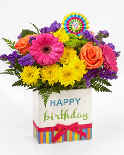 <p>This bouquet features a vivid combination of hot pink gerbera daisies, purple gilly flowers, yellow chrysanthemums, orange carnations, green button poms, and sprigs of bupleurum. Adding to the charm is a decorative ceramic vase, designed with colorful stripes, cheerful lettering, and a bright pink bow.</p>