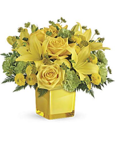 <p>This bouquet features sunny yellow roses and bright Asiatic lilies, paired with green carnations, yellow button spray chrysanthemums, and fresh bupleurum. Touches of leatherleaf fern add lush texture, while a clear glass cube vase offers a clean, modern presentation that lets the vibrant colors shine.</p>