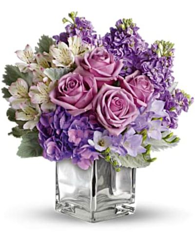 <p>This romantic mix features lush lavender roses, delicate white hydrangea, and soft stock blossoms, creating luxurious texture and gentle fragrance. The blooms are artfully arranged with subtle seasonal greens in a sleek, clear glass cube vase, offering a cool, modern presentation with a hint of frosty charm.</p>