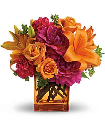 <p>Hot pink dahlias and carnations bring bold energy, while light orange roses and bright Asiatic lilies add warmth and radiance. The bouquet is accented with fresh green bupleurum and arranged in a modern orange glass cube vase that ties it all together with flair.</p>