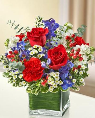 <p>This arrangement features a bold mix of red roses, deep blue delphinium, crisp white stock, vibrant red carnations, and clusters of red hypericum berries. Presented in a clear glass cube vase, the bouquet maintains a compact silhouette with a strong visual presence.</p>